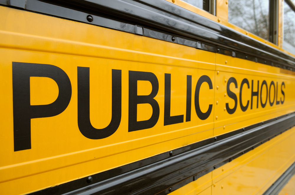 School bus background. Large "Public Schools" sign, black letters on yellow side panel
