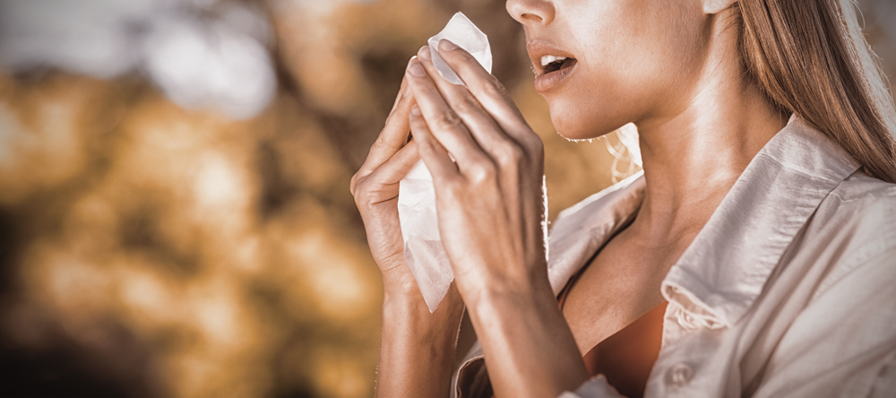 Beautiful woman using tissue while sneezing in park who is sick